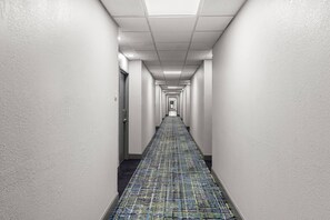 A long, narrow hallway with white walls and a patterned carpet. - Clarion Pointe Hinesville near Fort Stewart (Hinesville)