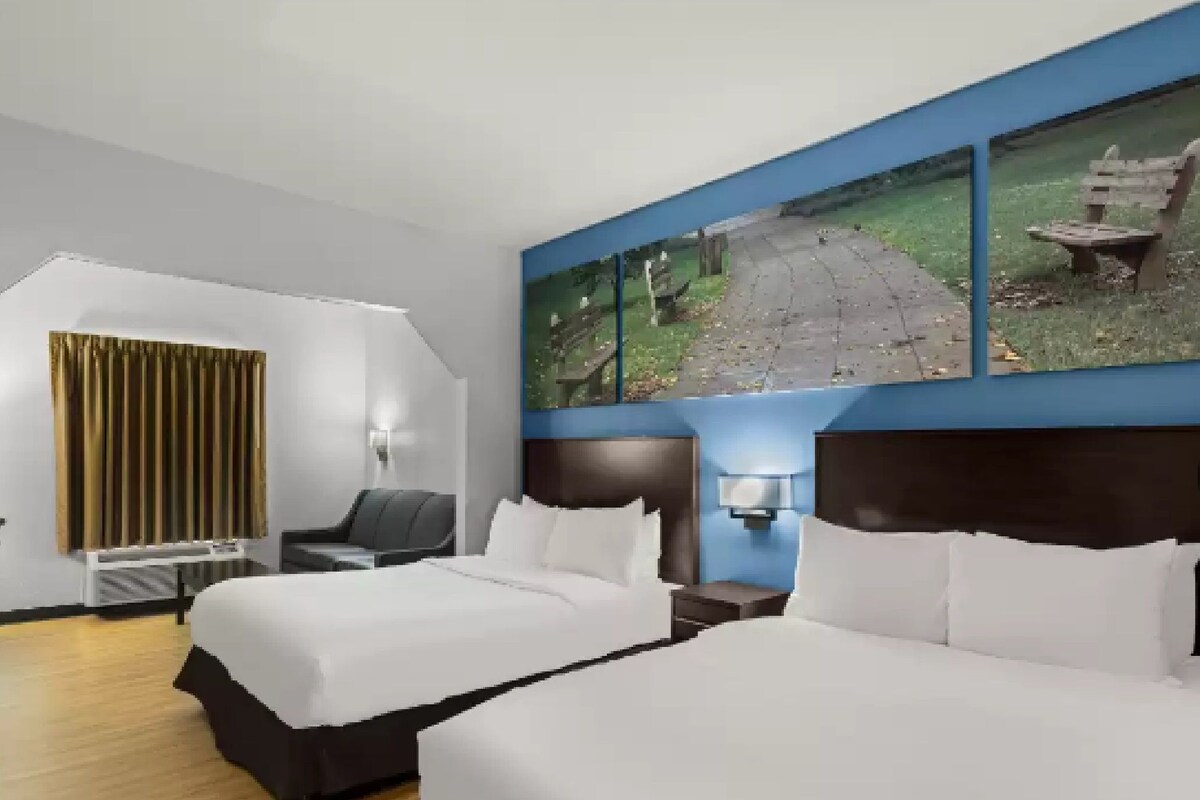 Ein Hotelzimmer mit Bett, Schreibtisch, Stuhl, einem Fenster mit Blick auf einen Park und einem Bild an der Wand.