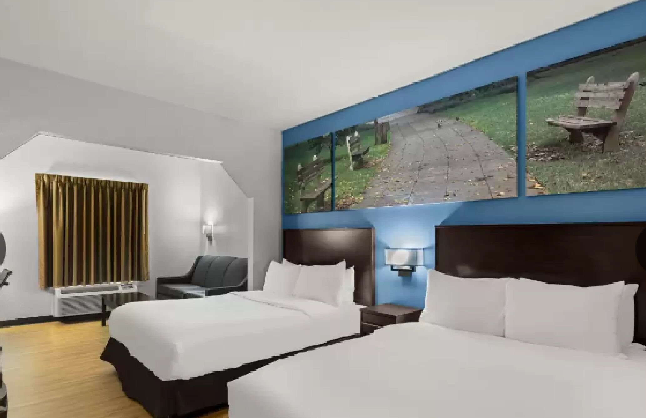 A hotel room with a bed, a desk, a chair, a window with a view of a park, and a painting on the wall.