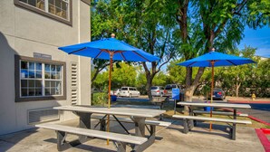 Outdoor picnic tables with blue umbrellas, a sign for 'Guest Laundry', and parked cars in the background. -  Studio 6 Deer Valley (Phoenix)