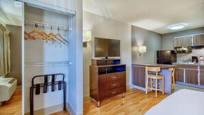 A hotel room with a wooden floor, a bed, a desk with a chair, a kitchenette, a TV, and a wardrobe with hangers. -  Studio 6 Deer Valley (Phoenix)