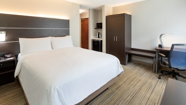 A hotel room with a large bed, a desk with a chair, a wardrobe, and a nightstand with a lamp. - Holiday Inn Express Hotel & Suites Downtown Minneapolis by IHG (Minneapolis)