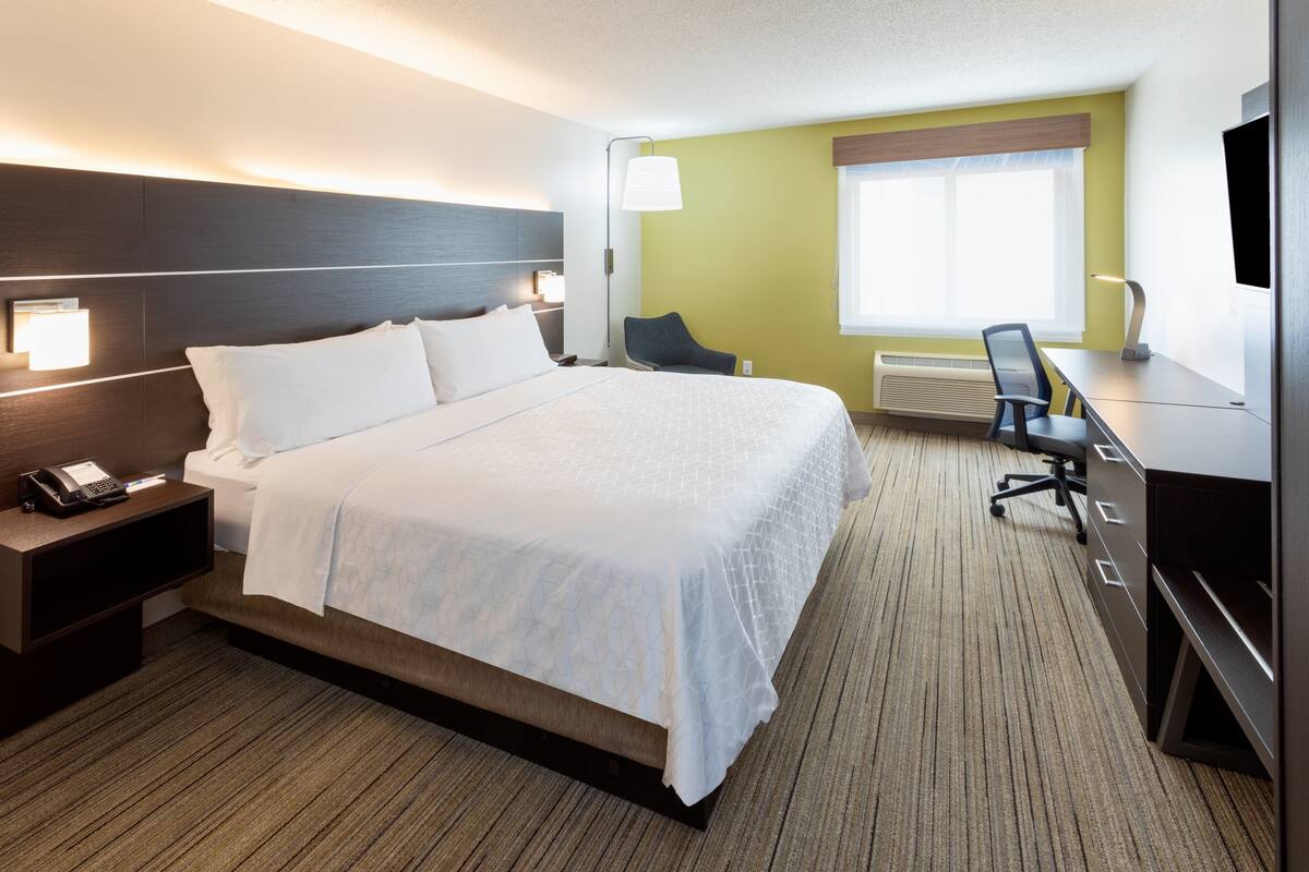 Une chambre d’hôtel dotée d’un grand lit, de tables de chevet, d’un bureau avec une chaise, d’une télévision à écran plat et d’une fenêtre offrant une vue agréable.