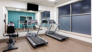 Une salle de sport équipée de tapis de course, d’un banc de musculation et d’un miroir.