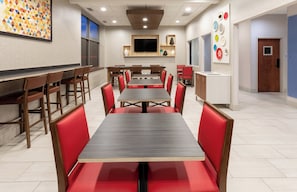 A dining area with multiple tables and chairs, a flat-screen TV mounted on the wall, and a patterned wall decoration.