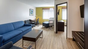 A modern hotel room with a blue sofa, a small table, a desk with a chair, and a bed with a headboard. - Holiday Inn Express Hotel & Suites Downtown Minneapolis by IHG (Minneapolis)