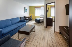 Une chambre d’hôtel moderne avec un canapé bleu, une petite table, un bureau avec une chaise et un lit avec une tête de lit.