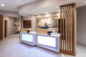 Zona de recepción de un hotel con diseño moderno, que incluye un mostrador de recepción, una pantalla digital y un panel de madera.