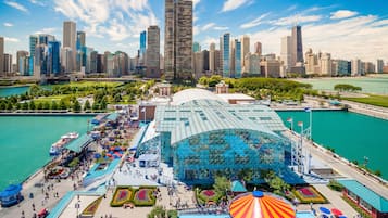 A large, modern building with a glass facade, surrounded by a park with walking paths and colorful umbrellas.