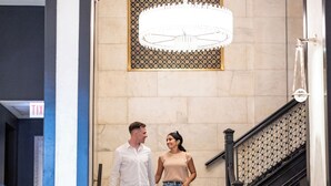A man and a woman walking down a marble staircase in a hotel lobby with a chandelier and a sign indicating an exit. - Silversmith Hotel Chicago Downtown (Chicago)