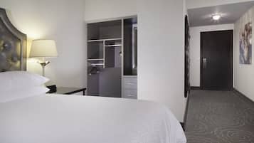 Een hotelkamer met een bed, nachtkastje, lamp, kast en een deur naar een andere kamer.