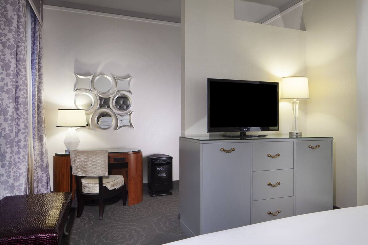 A hotel room with a bed, a television on a dresser, a desk with a chair, and a decorative wall with mirrors.