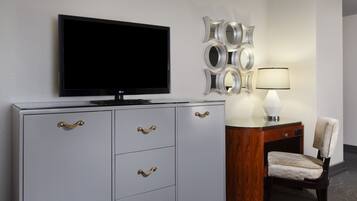Habitación de hotel con televisión de pantalla plana, minibar, escritorio de madera con lámpara y una silla.