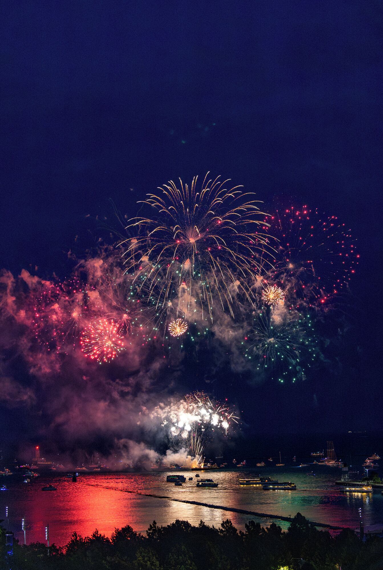 A nighttime view of a waterfront with fireworks display over the water.