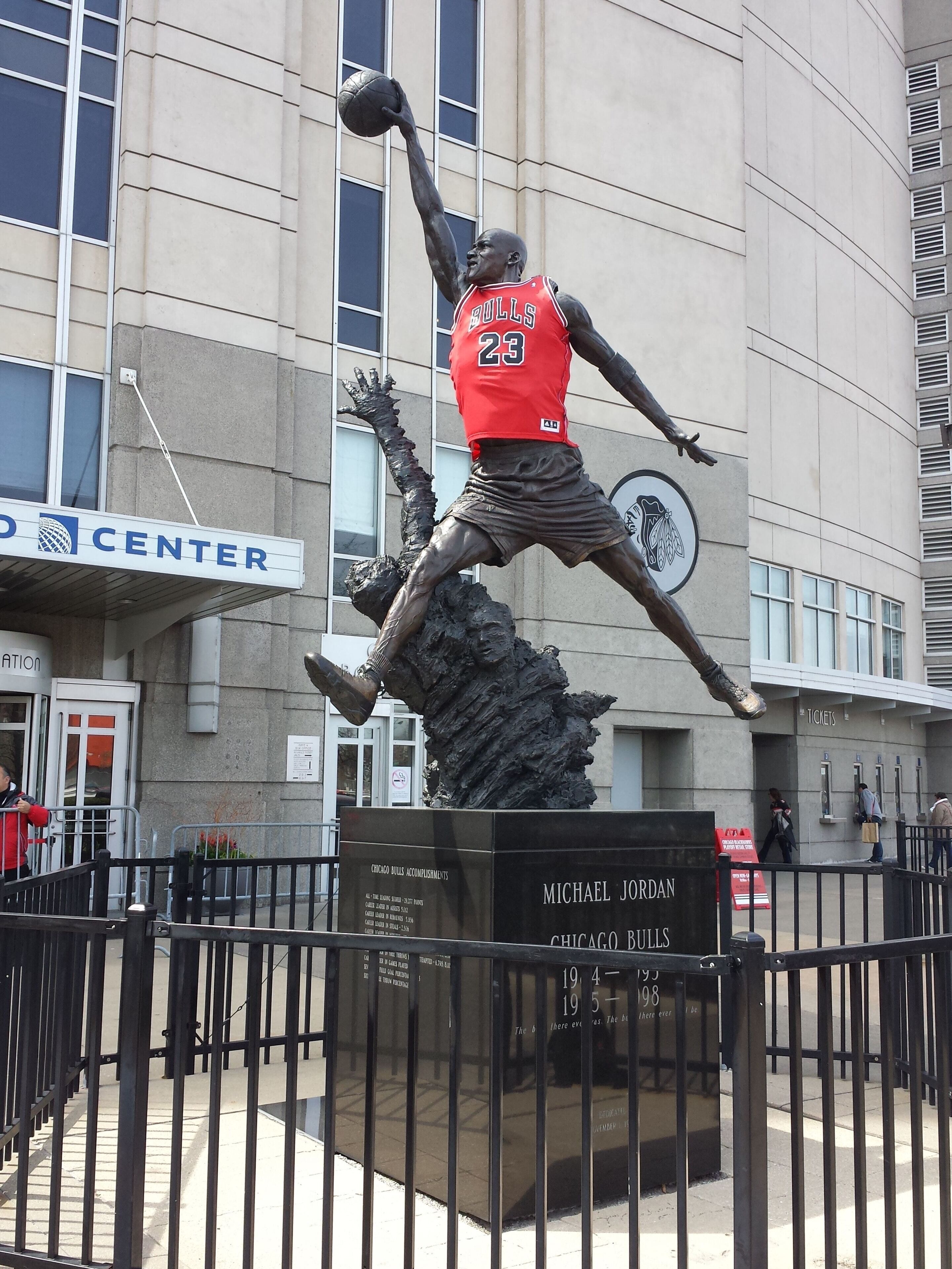 Una estatua de baloncesto de Michael Jordan con camiseta roja y el número 23, ubicada frente a un edificio con un letrero que dice 'CENTER'.