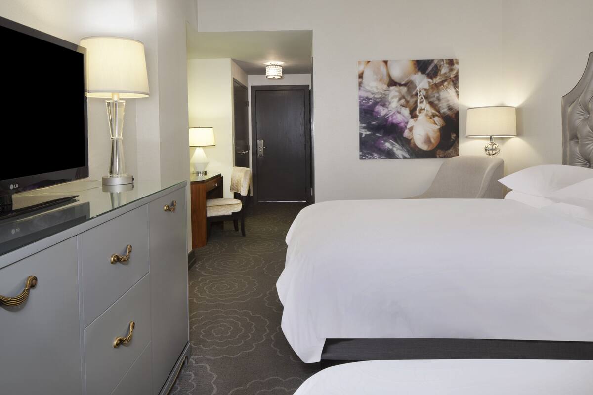 A hotel room with a bed, a TV, a desk with a lamp, and a chair.