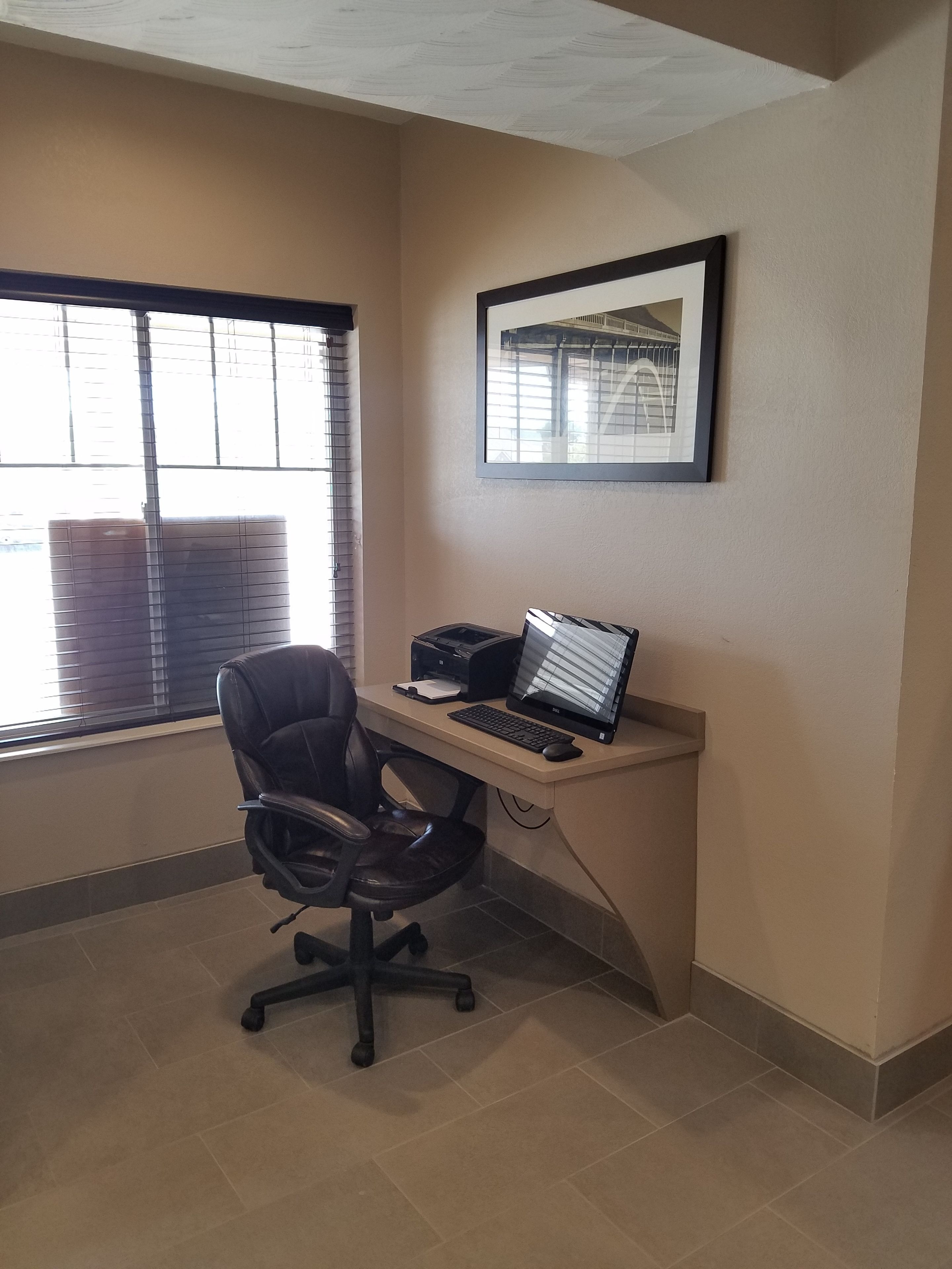 Un pequeño espacio de oficina con un escritorio, una silla, una computadora, una impresora y un cuadro en la pared.