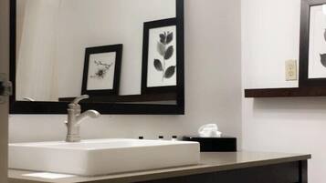 A bathroom with a white sink, a large mirror with lights, and a dark wooden vanity.