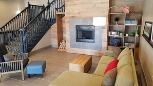 A modern living room with a staircase, a fireplace, a sofa, and a bookshelf. - Country Inn & Suites by Radisson, Indianapolis South, IN (Indianapolis)