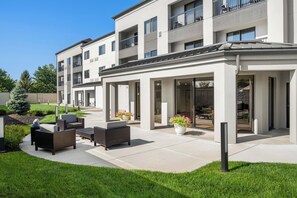 A modern apartment building with a covered outdoor patio area featuring outdoor furniture and potted plants. - Courtyard by Marriott Indianapolis South (Indianapolis)