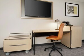 A hotel room with a desk, chair, TV, and a small refrigerator. - Courtyard by Marriott Indianapolis South (Indianapolis)