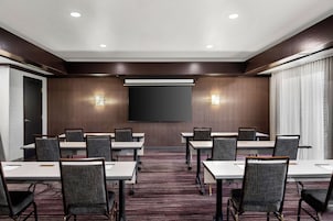 Sala de conferências com uma grande televisão de tela plana, várias mesas e cadeiras.