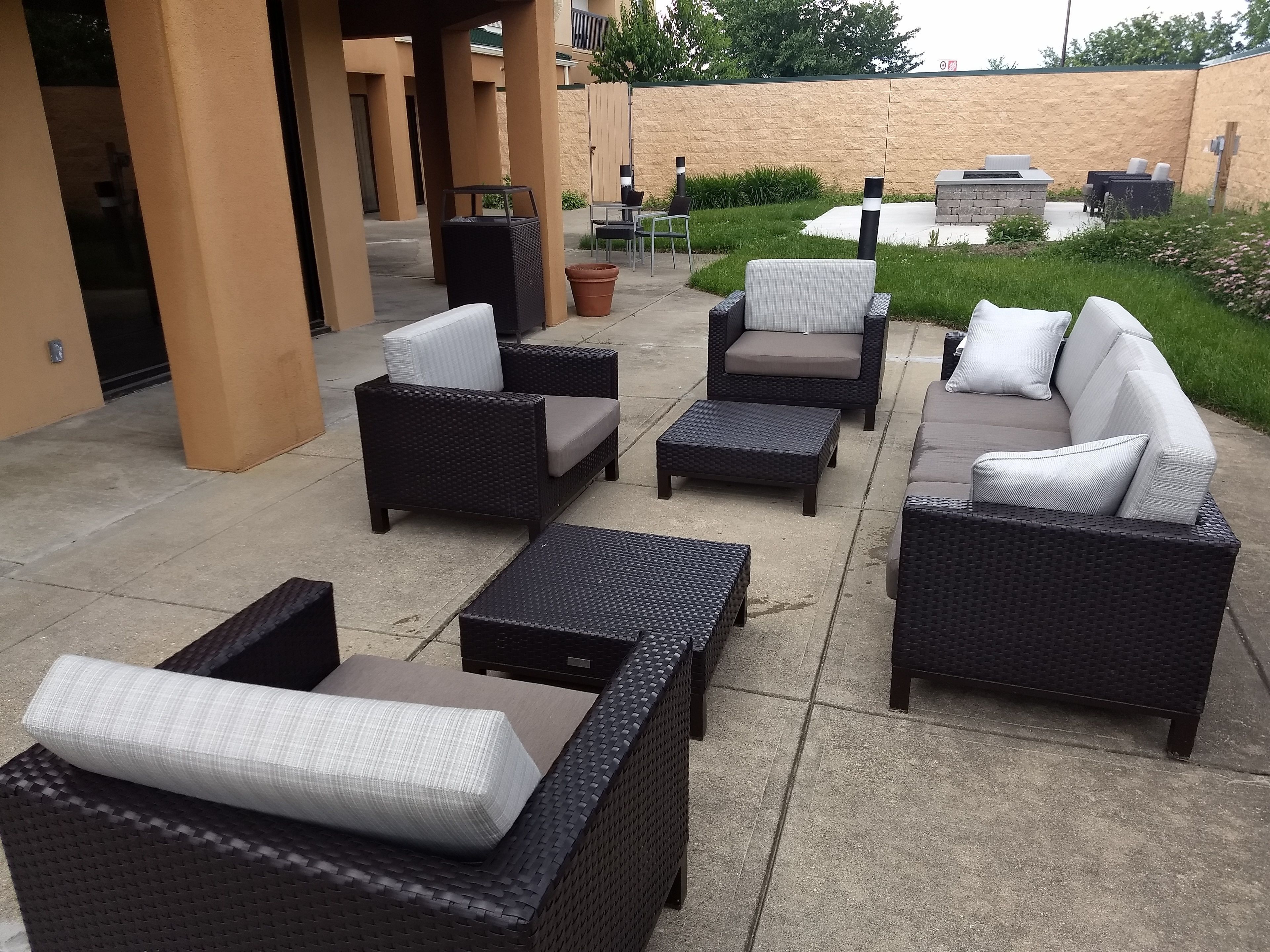 An outdoor patio area with wicker furniture, including sofas and ottomans, and a barbecue grill.