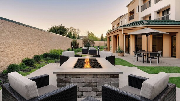 A courtyard with a stone fire feature, wicker furniture, and a building with outdoor seating. - Courtyard by Marriott Indianapolis South (Indianapolis)