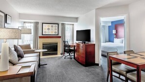 A hotel room with a sofa, a desk, a fireplace, a television, a dining table, and a bed. - Residence Inn by Marriott Denver North-Westminster (Westminster)