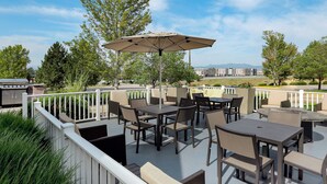 An outdoor patio with tables and chairs, a grill, and a view of buildings in the distance. - Residence Inn by Marriott Denver North-Westminster (Westminster)