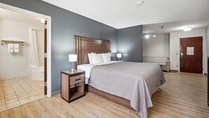 A modern hotel room with a large bed, a nightstand, a wooden headboard, and a bathroom visible through an open door. - Quality Inn & Suites Dawsonville (Dawsonville)