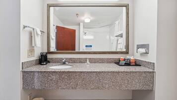 A bathroom with a granite countertop, a sink, a mirror, a towel rack, a coffee maker, and toiletries.