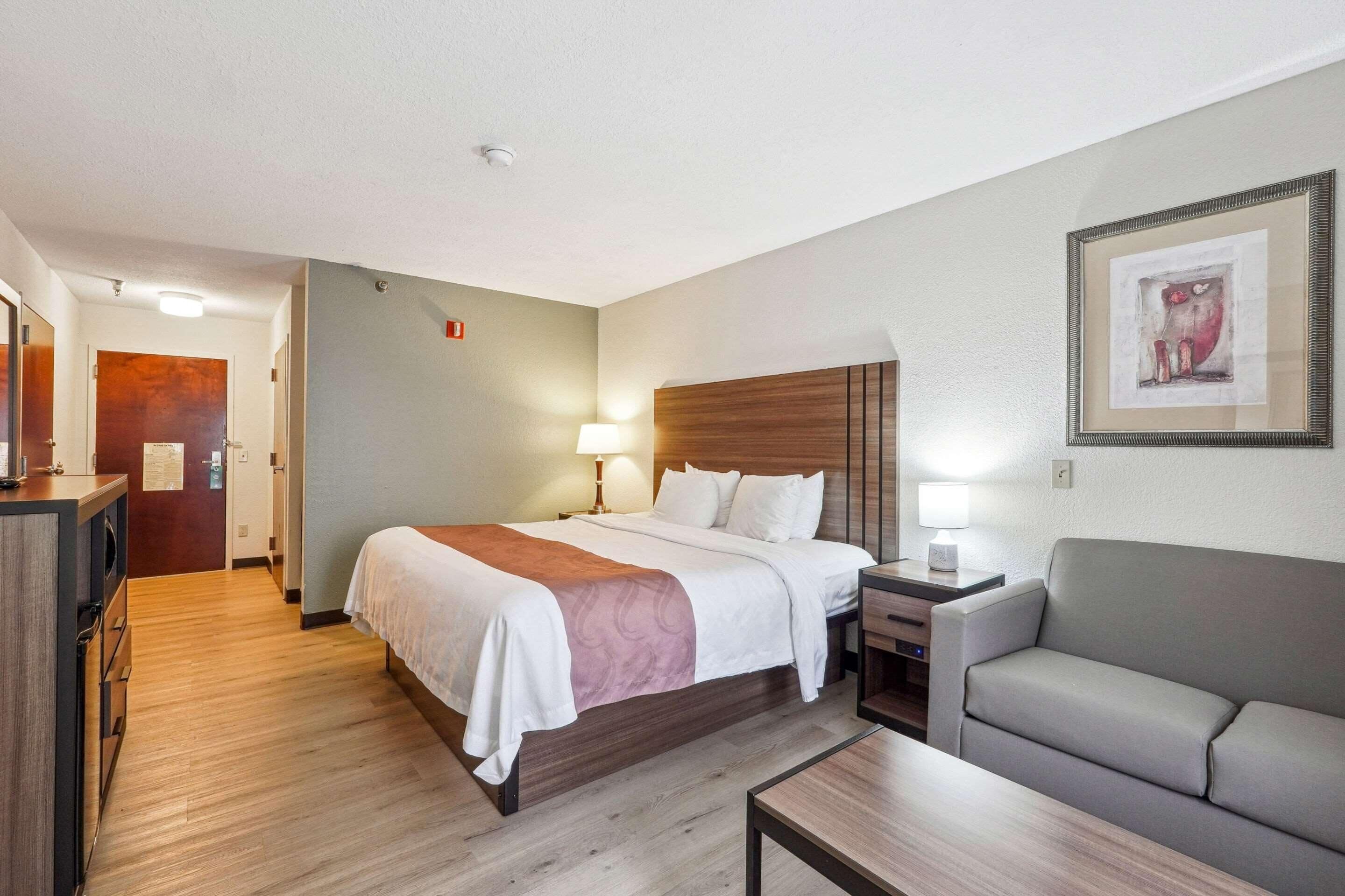 Una habitación de hotel con cama, mesita de noche, lámpara y sofá.