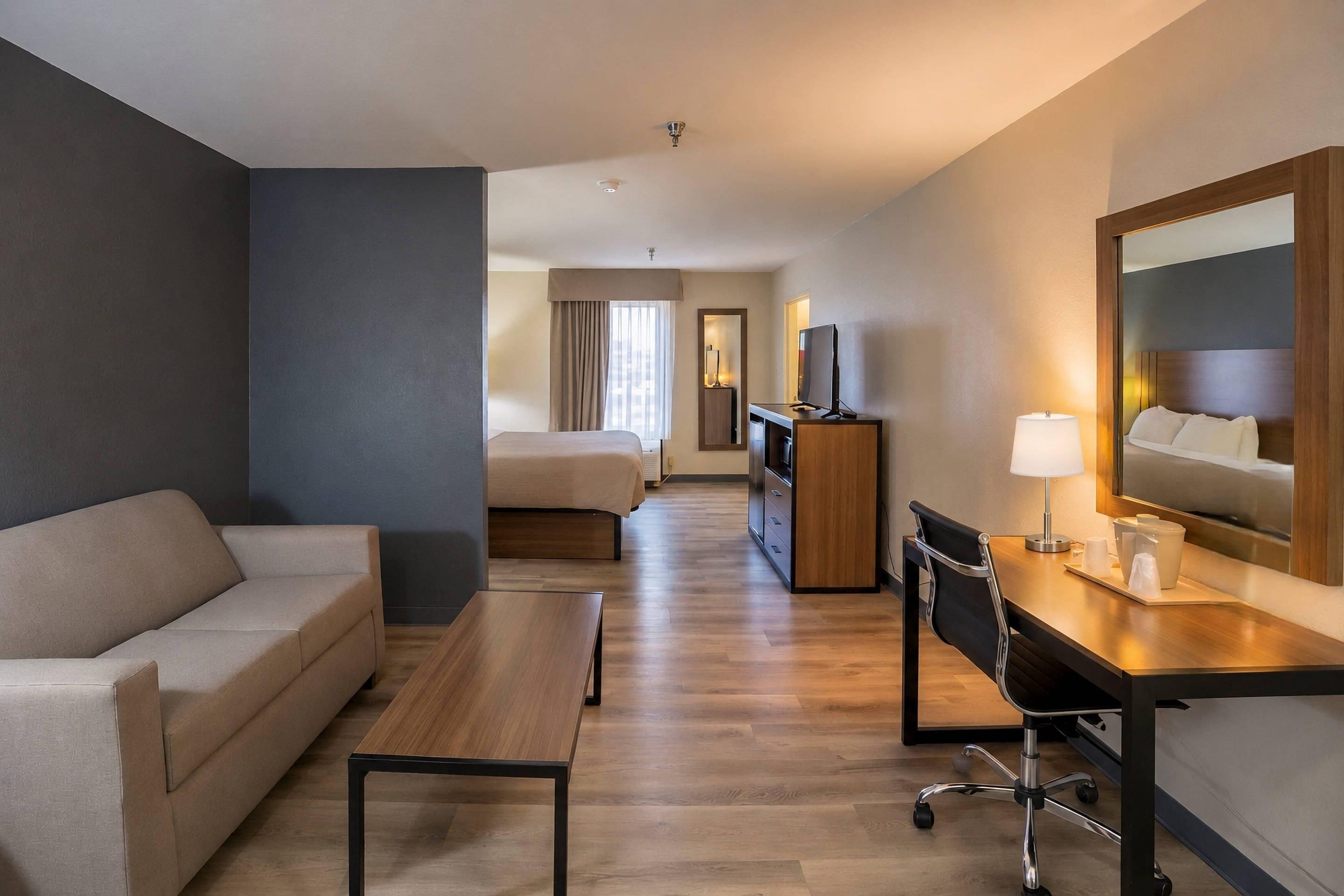 A hotel room with a bed, a desk with a chair, a sofa, and a large mirror.