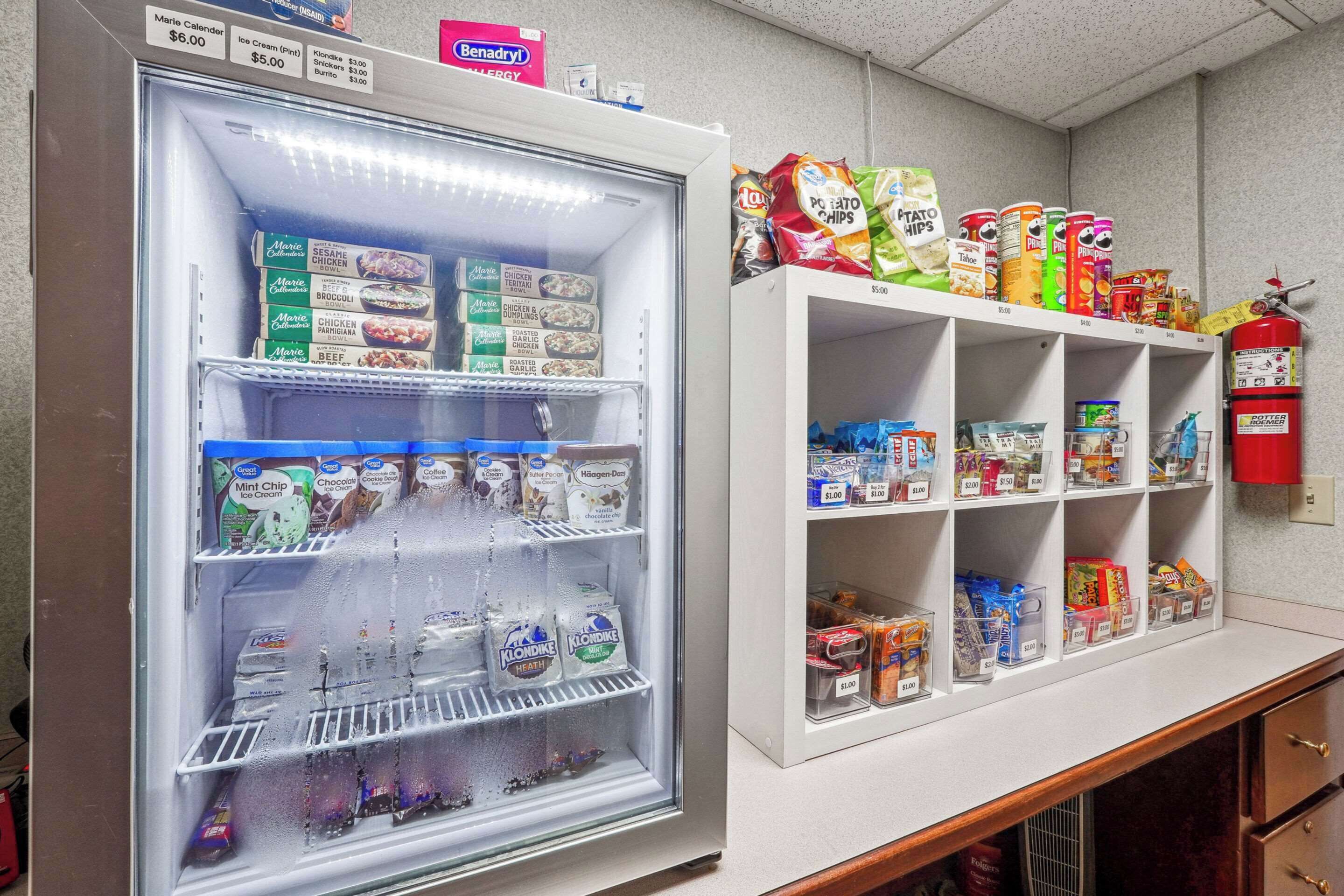 Un distributeur automatique rempli de collations et de boissons, un extincteur fixé au mur et une étagère contenant des produits emballés.