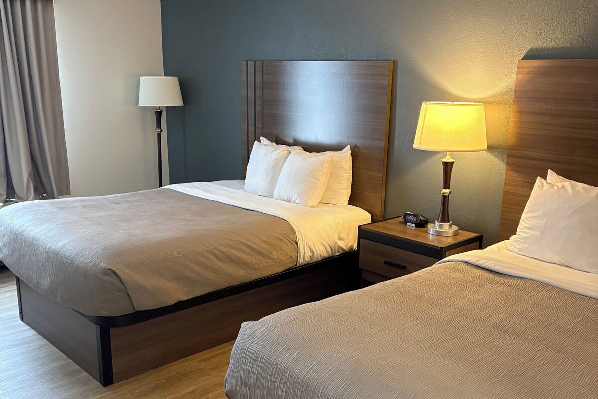 A hotel room with two beds, a nightstand with a lamp, and a view of the city.