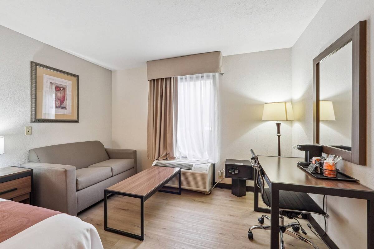 A hotel room with a sofa, a small table, a desk with a lamp, a chair, and a large mirror.