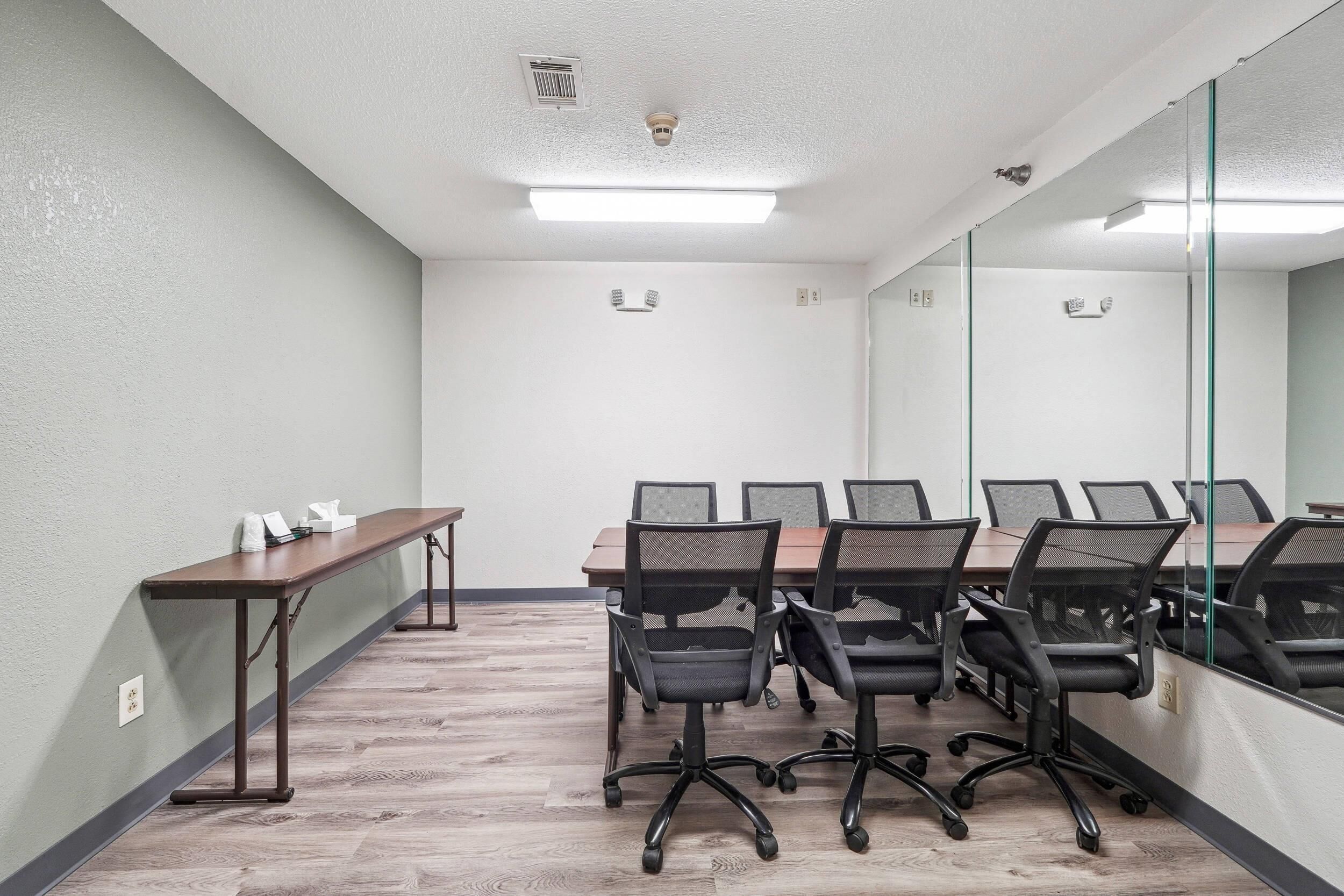 A conference room with a long table, several chairs, a small side table, and a large mirror on one wall.