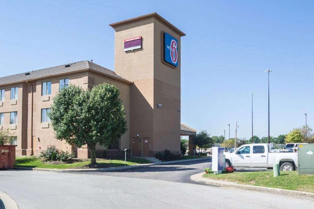 A hotel with a prominent sign, a parking lot, and a tree in front.
