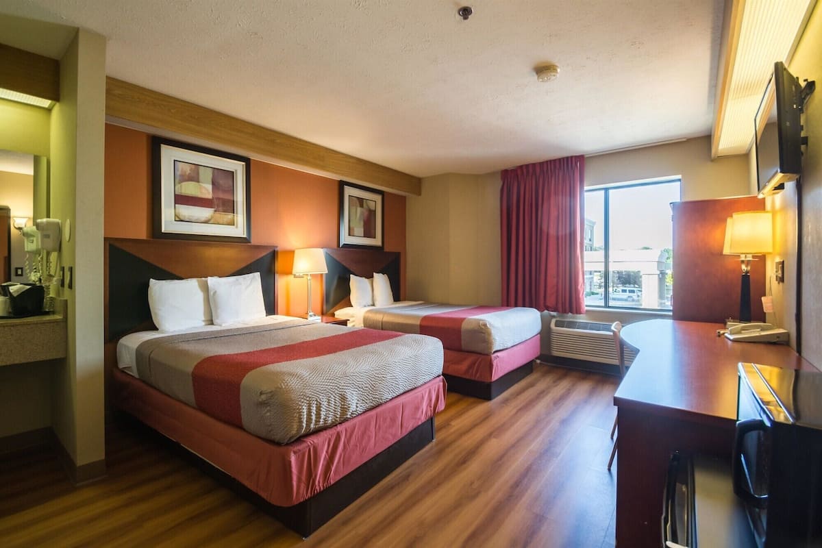 A hotel room with two beds, a desk, and a window.