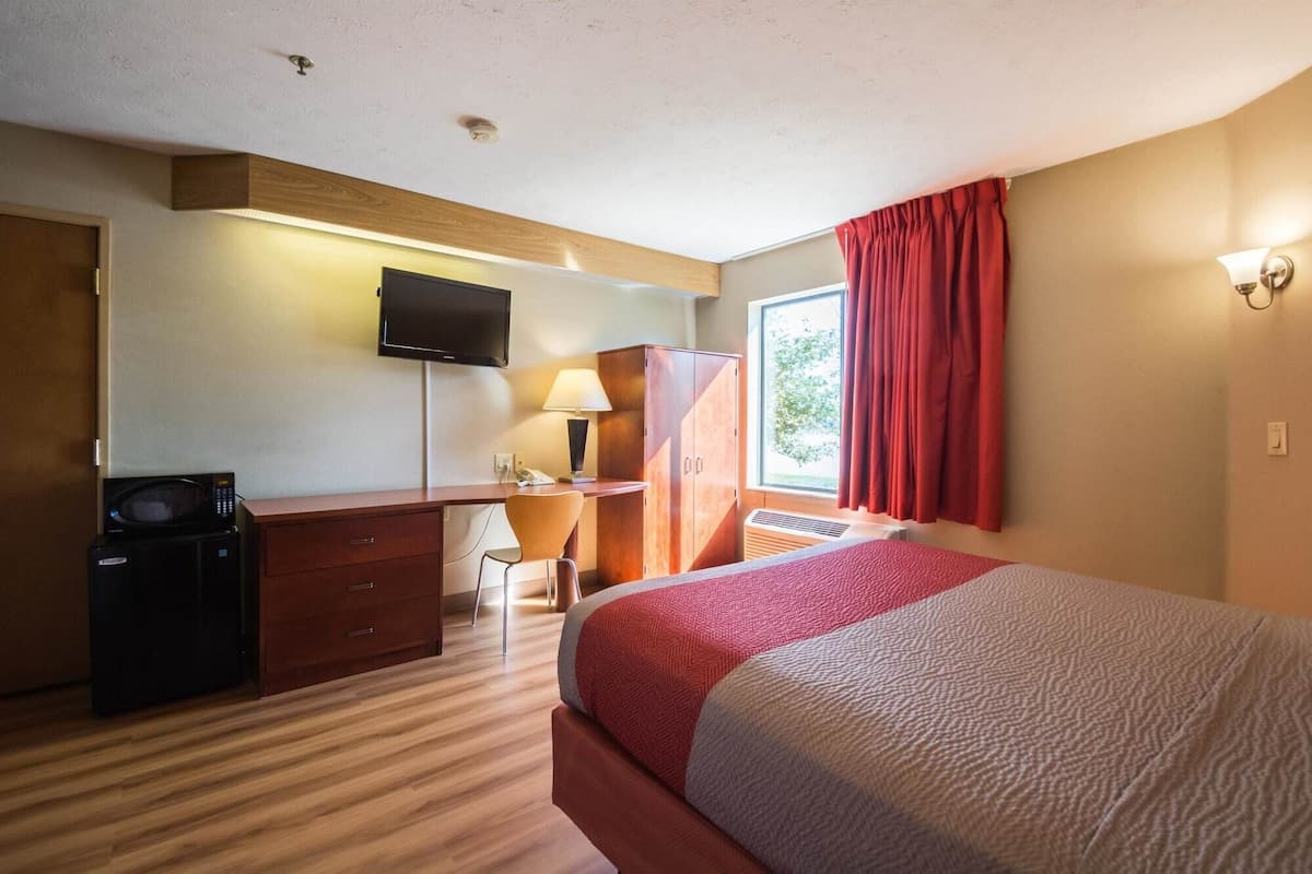 A hotel room with a bed, a desk with a computer, a TV, and a microwave.