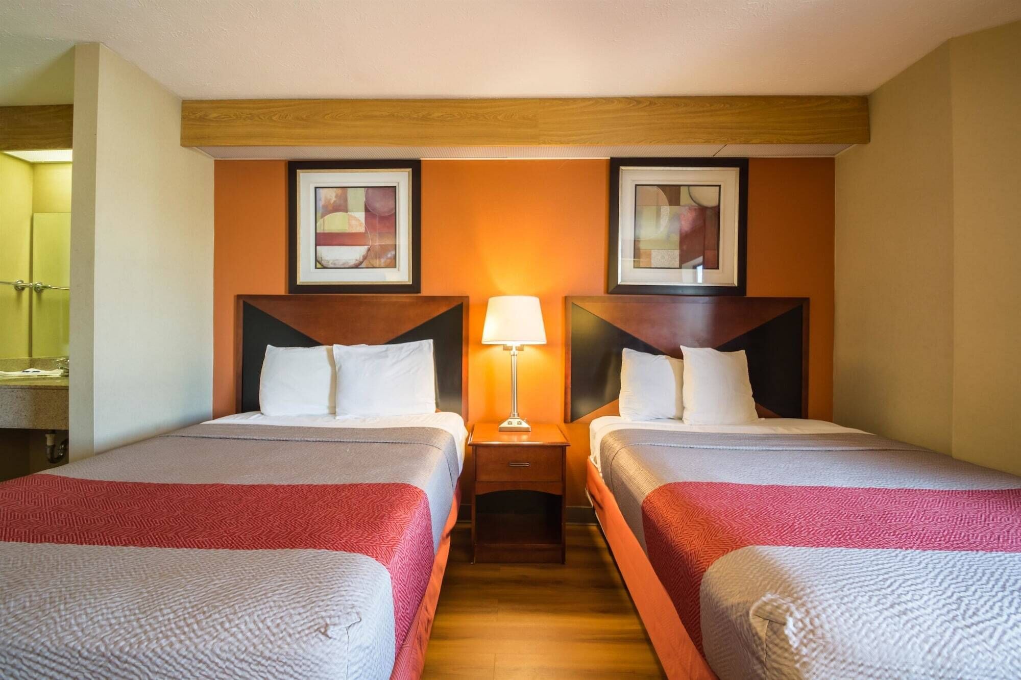 A hotel room with two beds, a nightstand with a lamp, and two framed pictures on the wall.