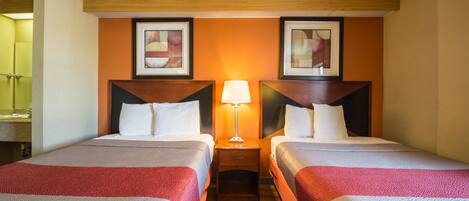 A hotel room with two beds, a nightstand with a lamp, and two framed pictures on the wall.