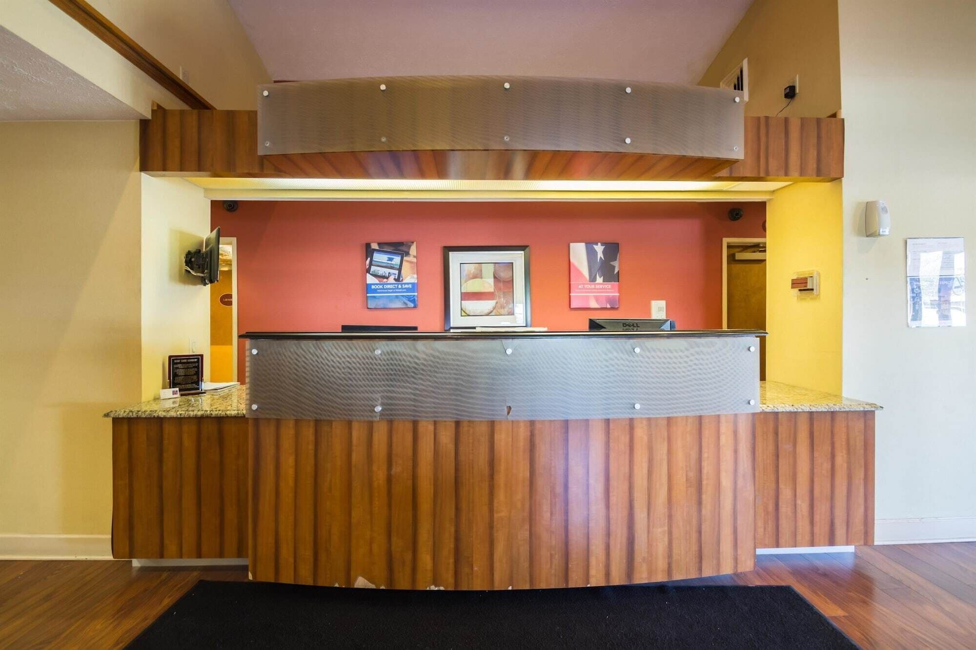 Un comptoir d’accueil avec un revêtement en bois, un plan de travail en métal et un mur rouge orné d’œuvres d’art encadrées et d’une enseigne.