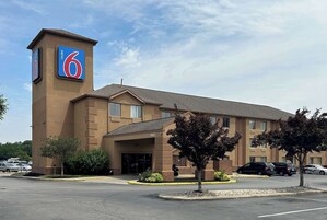 Un motel con un llamativo letrero con el número '6', un estacionamiento y la entrada al edificio.