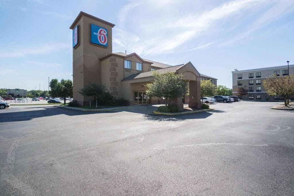 A motel with a prominent sign, a parking lot, and a building in the background.