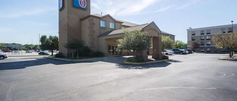 A motel with a prominent sign, a parking lot, and a building in the background.