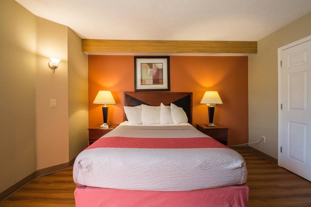 A hotel room with a bed, two bedside lamps, a framed picture on the wall, and a door.