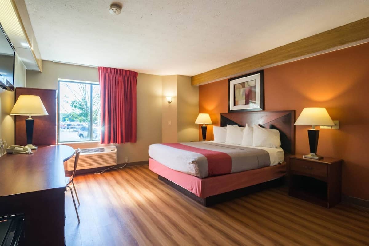 A hotel room with a bed, bedside tables, a desk, and a window with curtains.