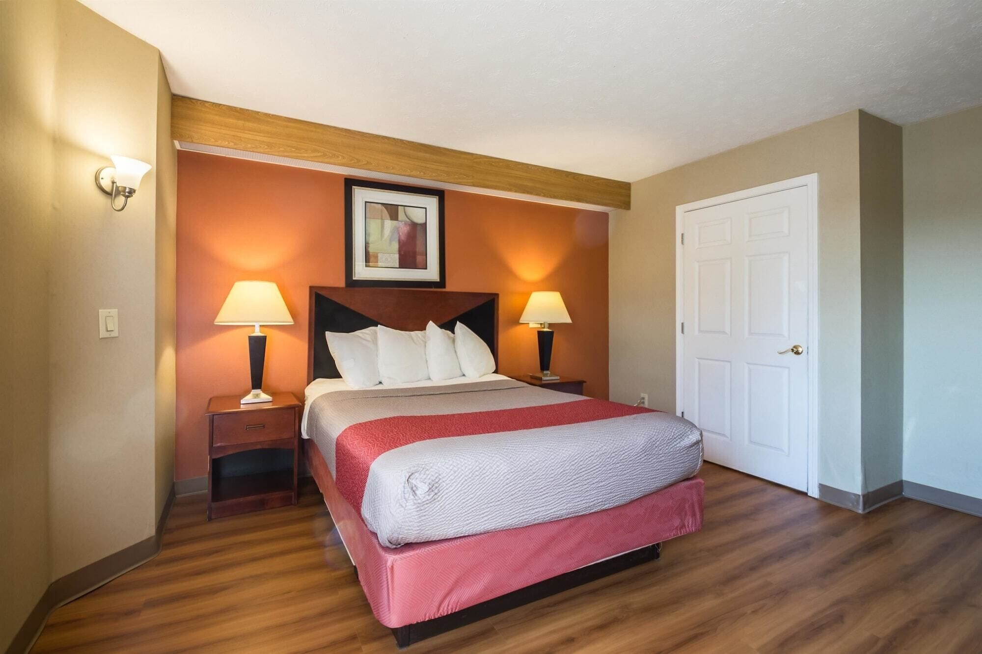 A hotel room with a bed, two bedside lamps, a framed picture on the wall, and a white door.